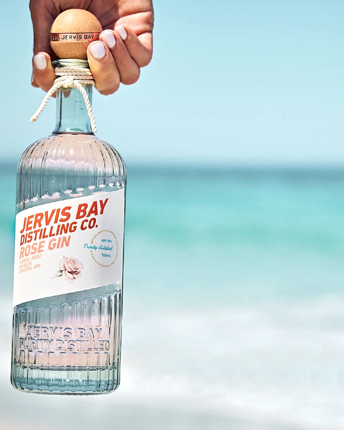 Beautiful image of craft gin being held in front of a blue Australian beach.